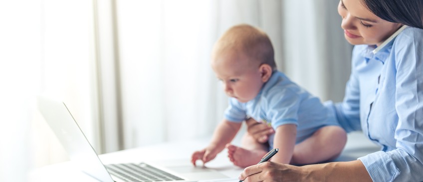 Frau sitzt mit Baby am Laptop